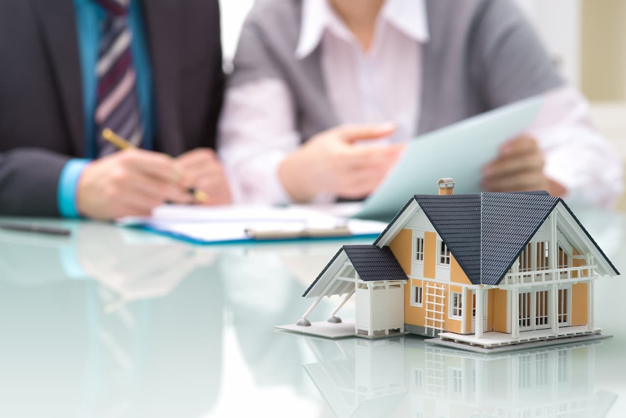 A model replica of a home on a glass desk. Two office people in the background.